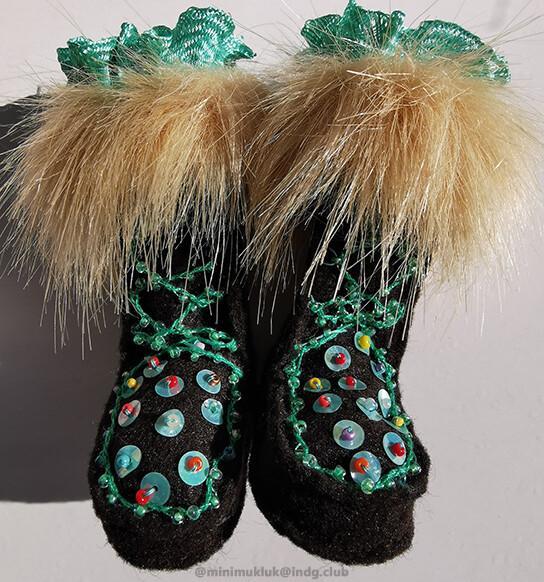 A close up photo of two hand sewn mukluk boots. Blue embroidery thread for lace and matching trim. Light brown (faux) fur for contrast. Brown felt for the exterior of each. Multi colored beads dot each foot panel. These mukluk are made for winter or spring.