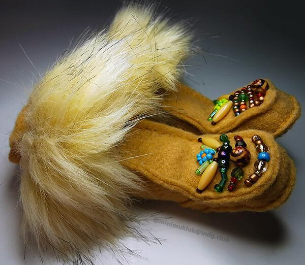 Laying on their sides..a miniature pair of beaded brown tan  winter boots. Tufted and very fluffy faux fur. Created from the magical beasts at the fabric shop. Various beads embellish each. Two beaded flowers are the center of both pairs.
