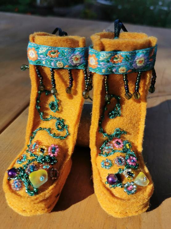 Two miniature mukluk boots. Orange felt with flower beaded foot panels. Each panel with colorful beaded flowers and green garland stems. Glass bead has been chosen for translucence and shine.