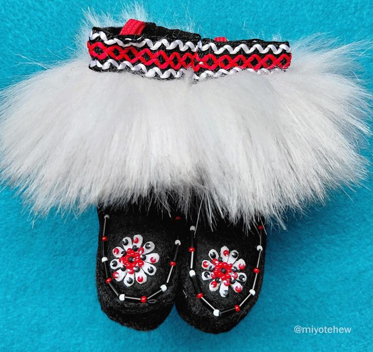 A pair of beaded felt black boots. Small white felt petals with red and black beads. Matching trim and white fur.