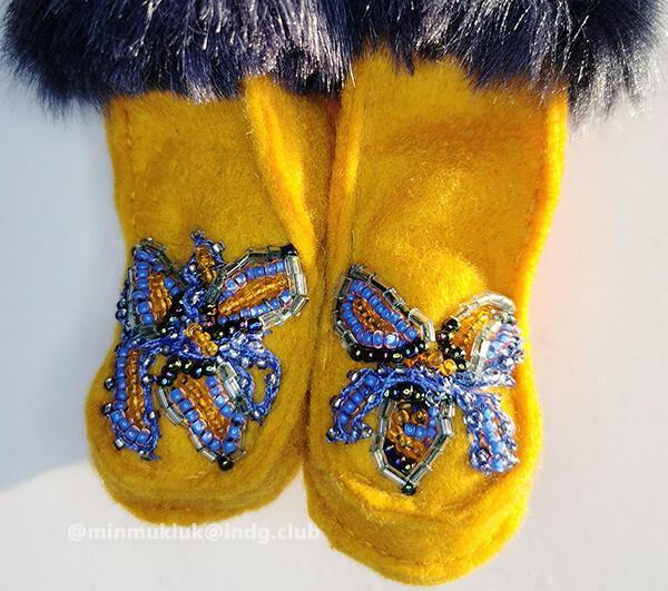 Photo of two miniature fur boots. Hand sewn with blueish grey (faux) fur with yellow felt. Beaded on each foot panel are two butterfly shapes with flowers. Blue and orange, clear and metallic beads create flash and shine in a tiny space.